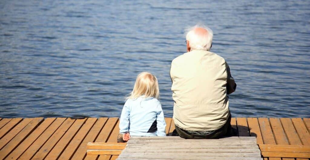 elderly man and young girl sitting on bench looking out at sea